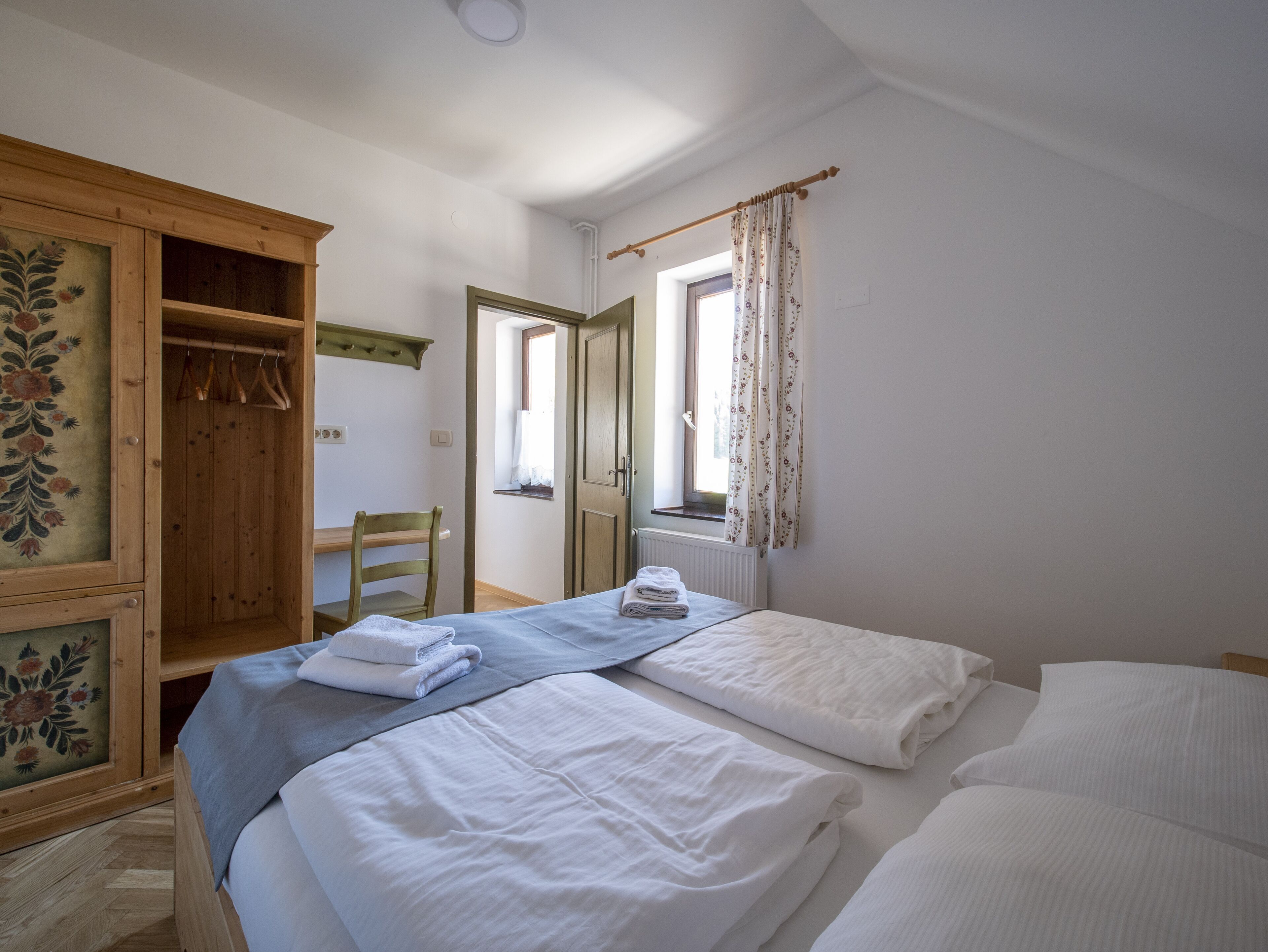 Un dormitorio con dos camas, un armario de madera, una silla y una ventana con cortinas.