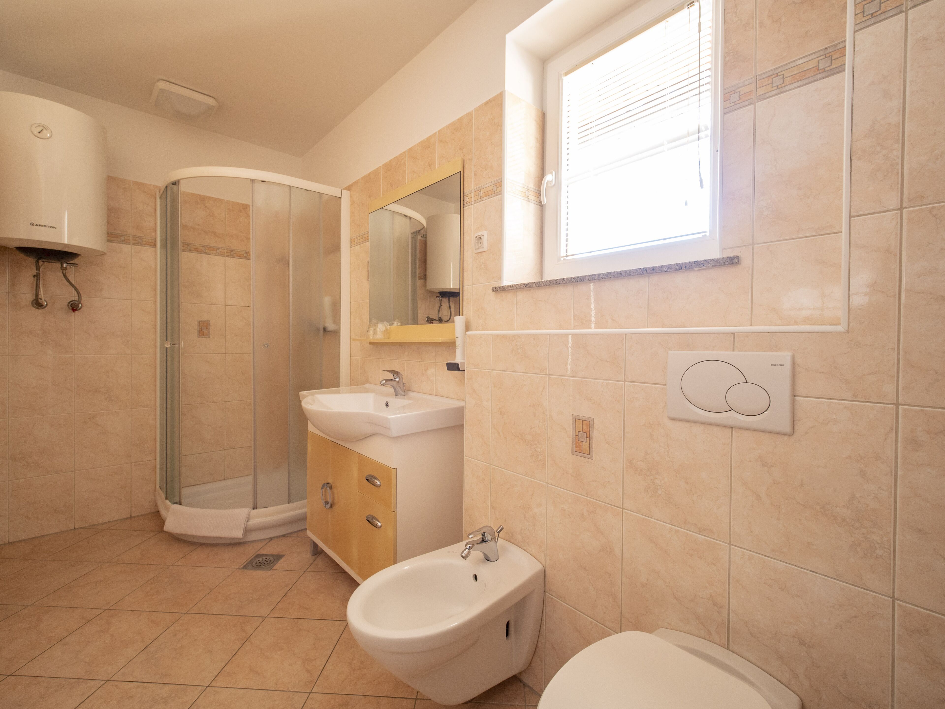 A bathroom with a shower, sink, bidet, toilet, and a window.