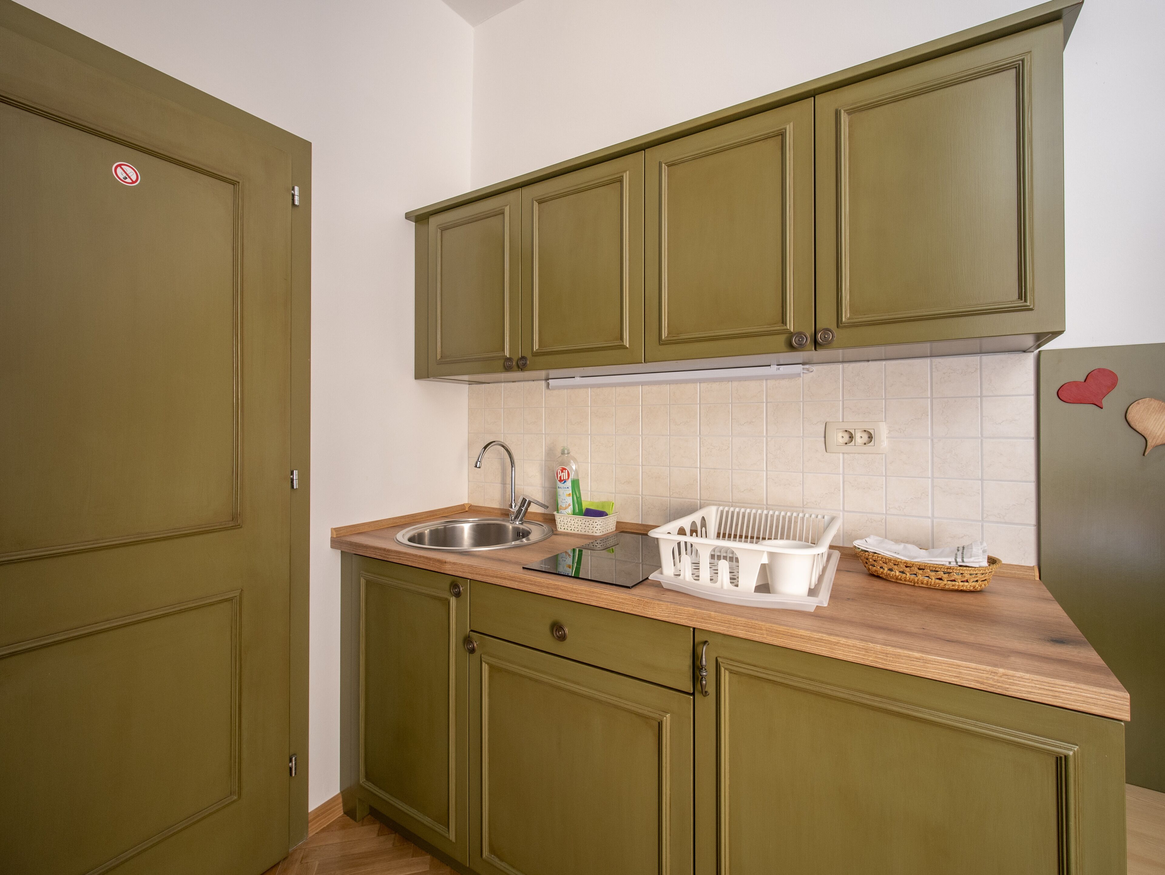 A kitchen with green cabinets, a stainless steel sink, and a wooden countertop.