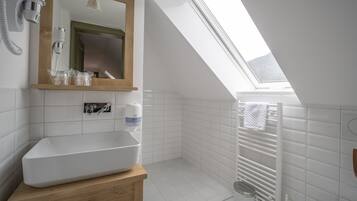 Un baño moderno con tragaluz, baldosas blancas, tocador de madera, inodoro y barra para toallas.