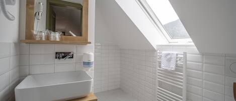 A modern bathroom with a skylight, white tiles, a wooden vanity, a toilet, and a towel rack.