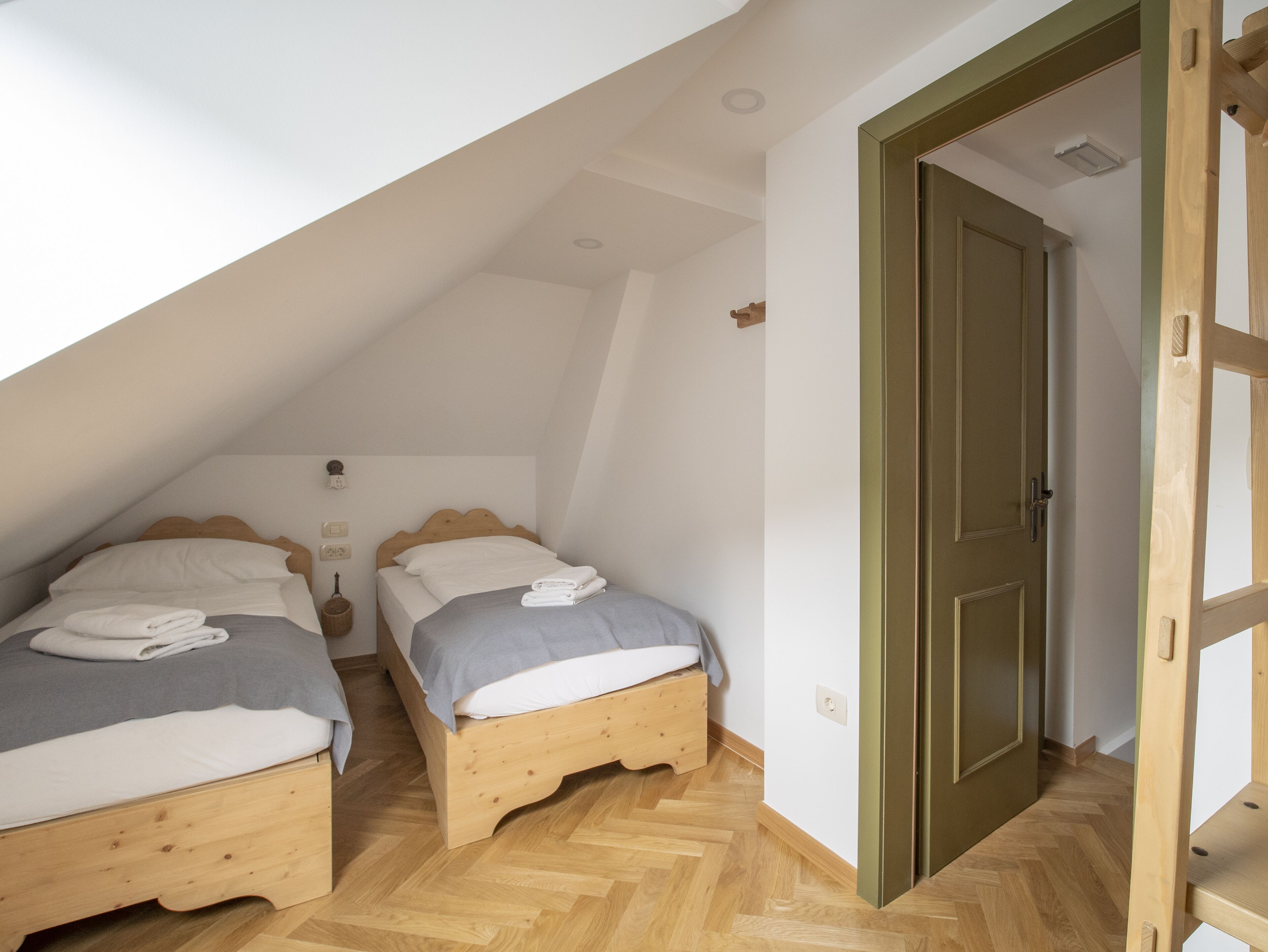 Una habitación pequeña y acogedora con dos camas de madera, una puerta de madera y un suelo con motivo de espiga.