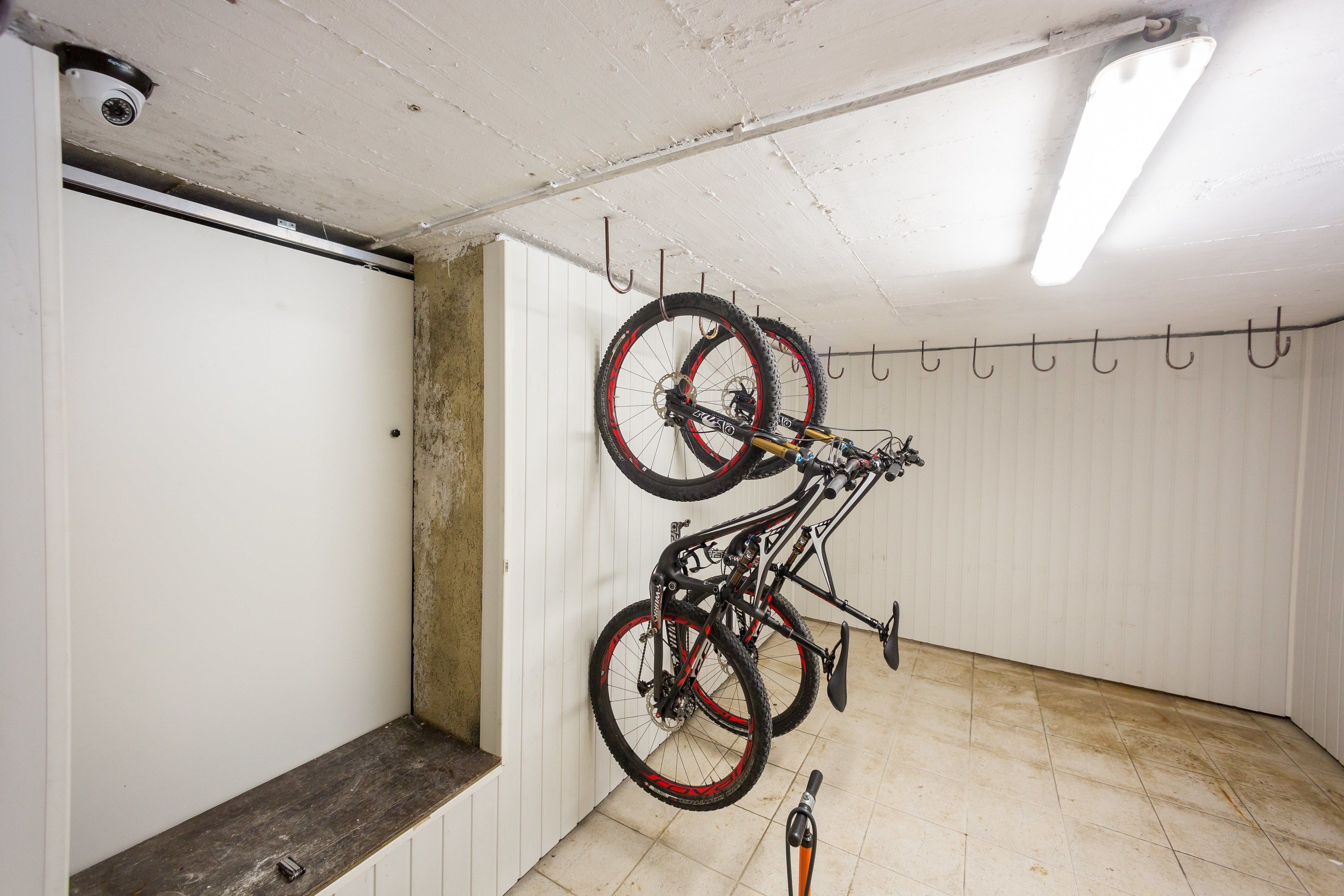 Una habitación con una puerta blanca, un banco y un perchero para bicicletas fijado a la pared, con dos bicicletas.