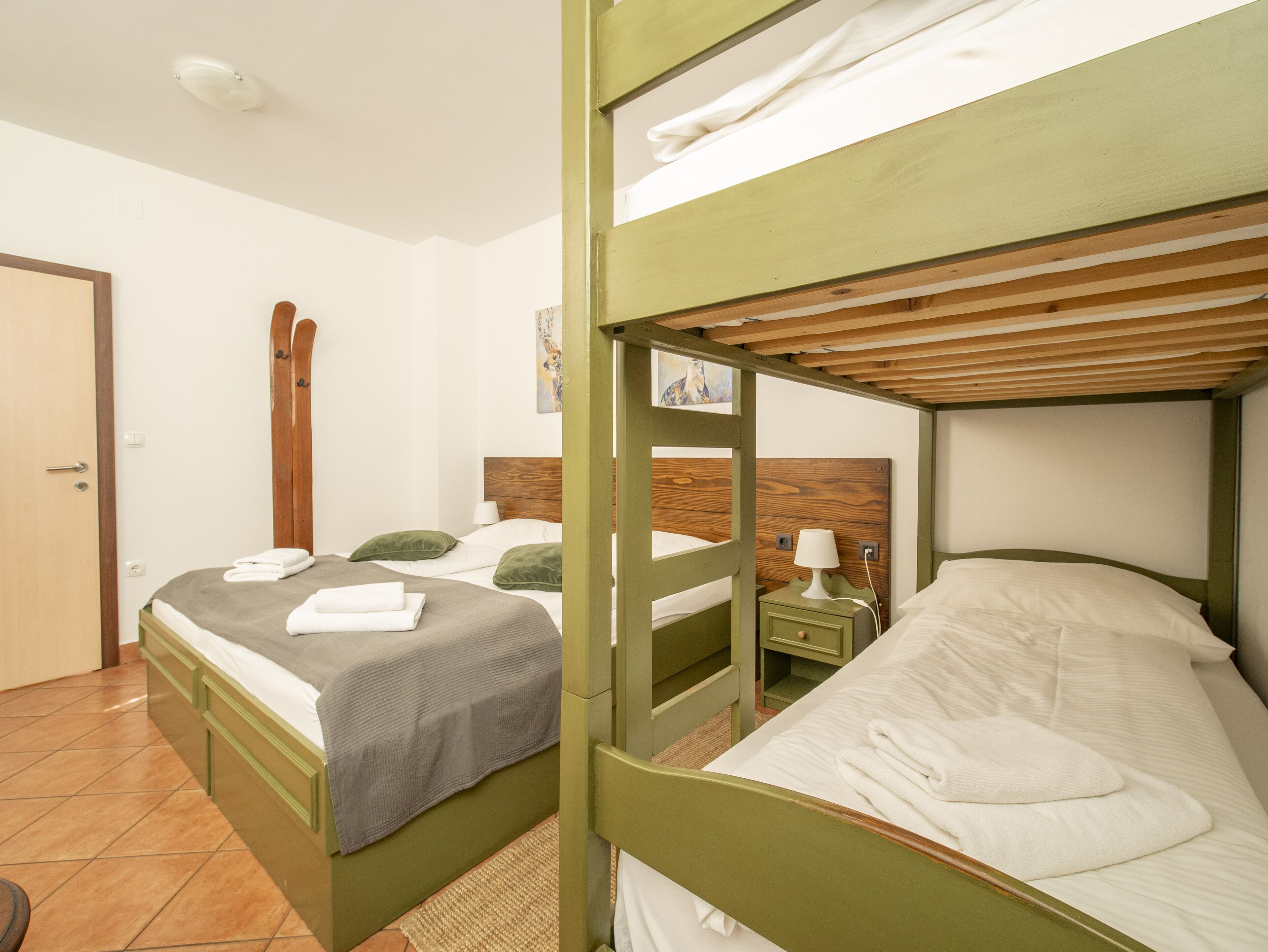 A room with two bunk beds, a wooden headboard, a bedside table with a lamp, and a painting on the wall.