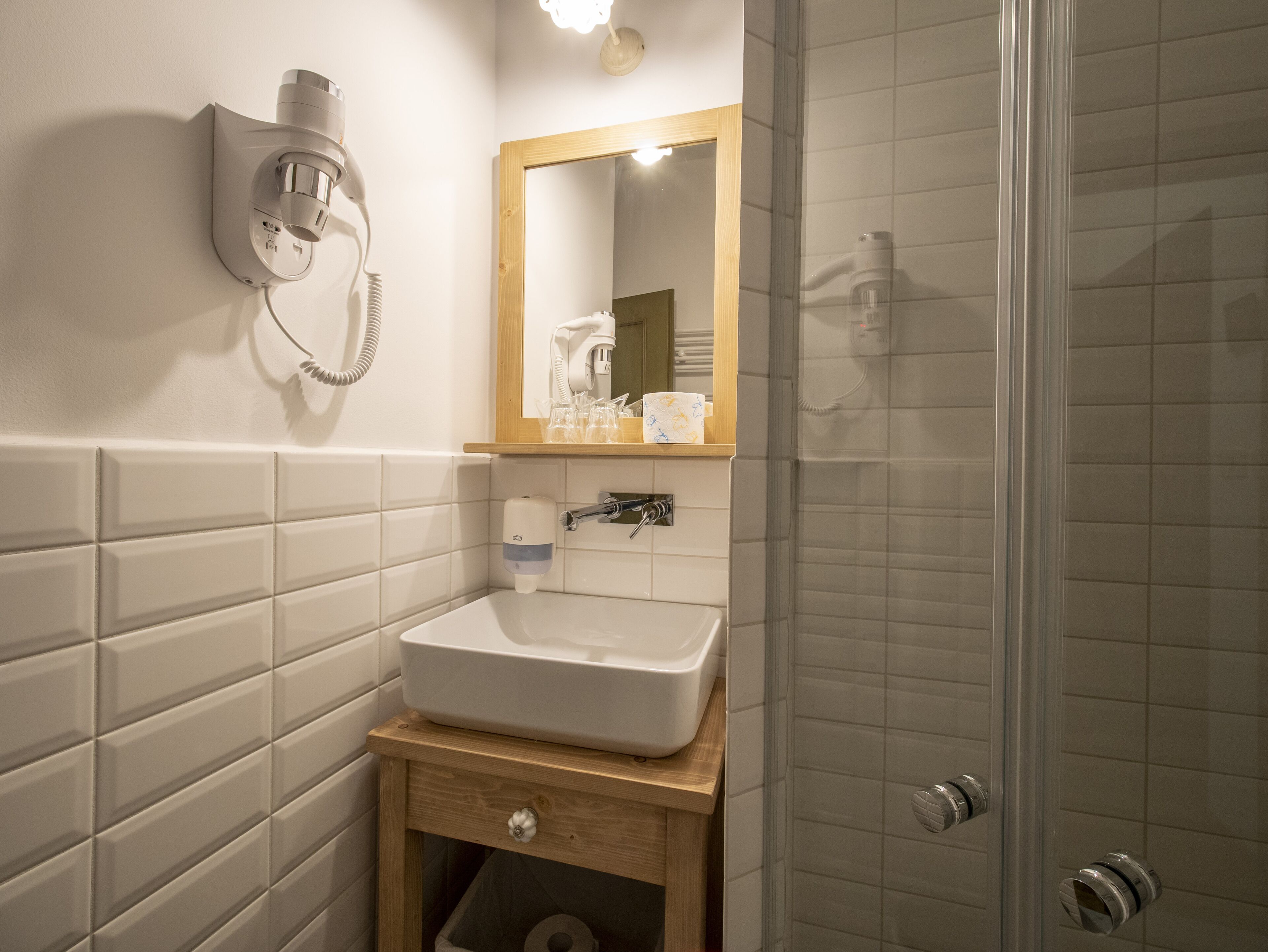 A bathroom with a white sink, a wooden vanity, a mirror, and a shower area.