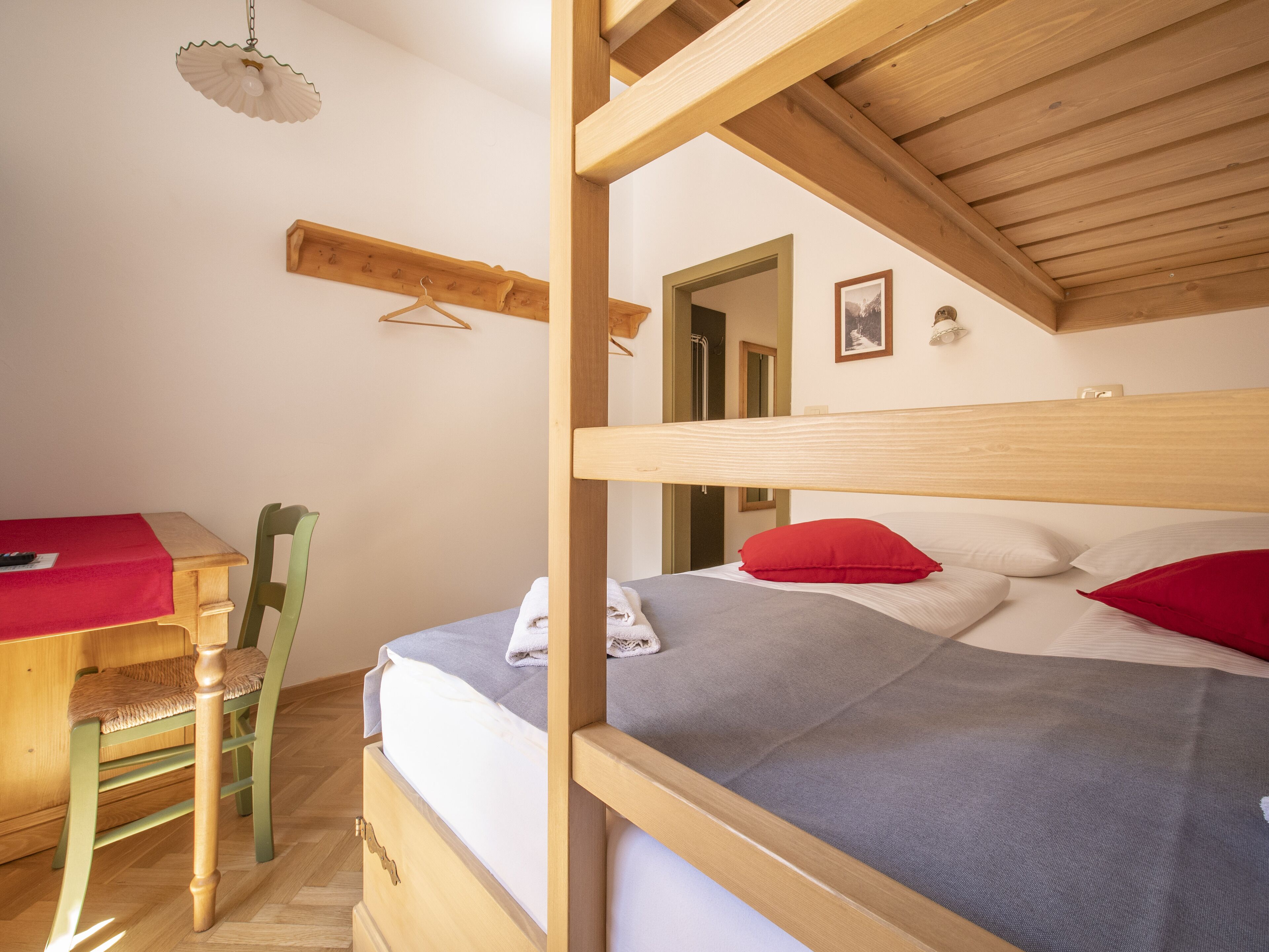 Une chambre avec un lit superposé, un bureau recouvert d’une nappe rouge, une chaise et un luminaire suspendu.