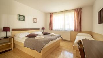 A hotel room with a large bed, a bedside table, a chair, a window with curtains, and a radiator.