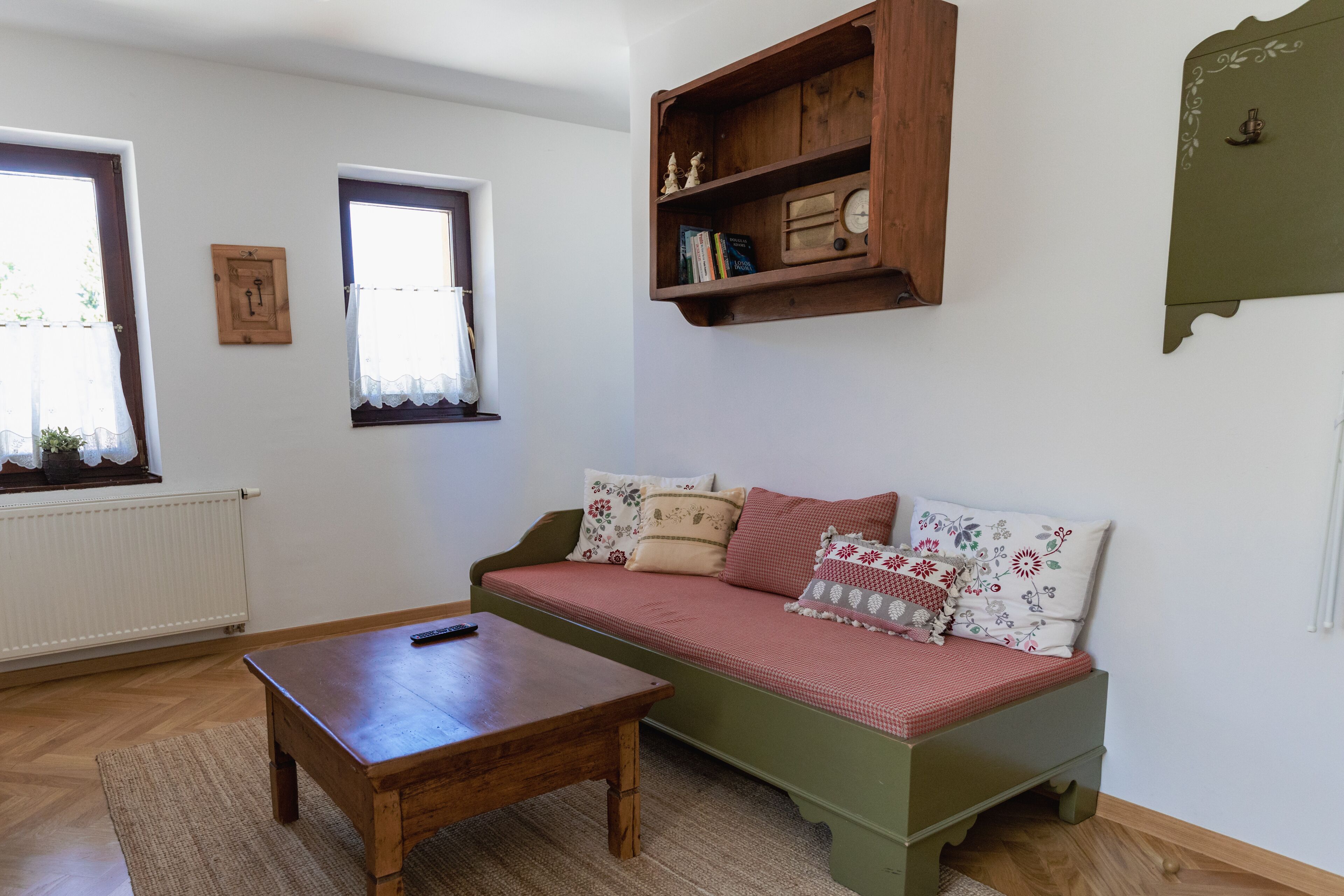 A cozy room with a green sofa, a wooden table, and a shelf with decorative items.