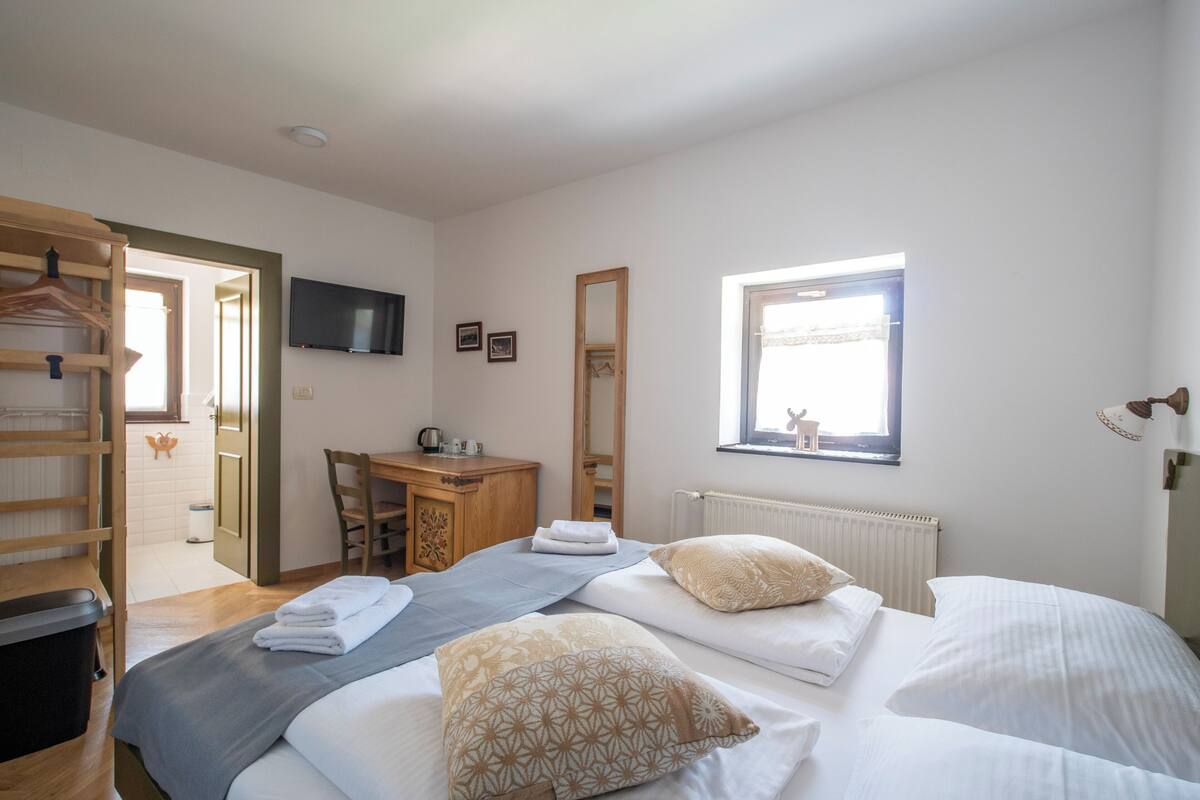 Habitación de hotel con dos camas, un escritorio, una silla, un televisor y una ventana con vista a un ciervo.