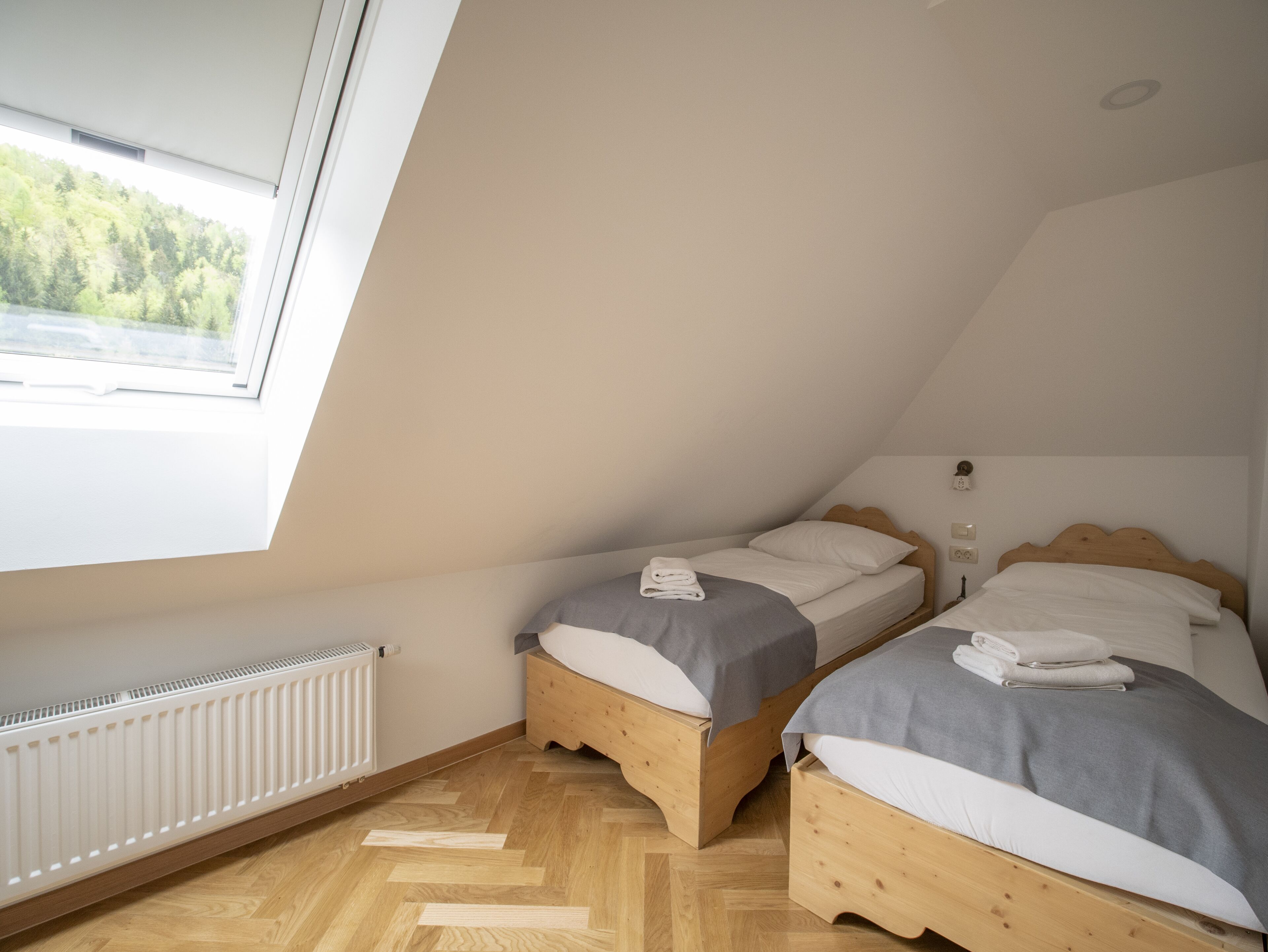 A bedroom with two wooden beds, a radiator, and a window with a view of trees.