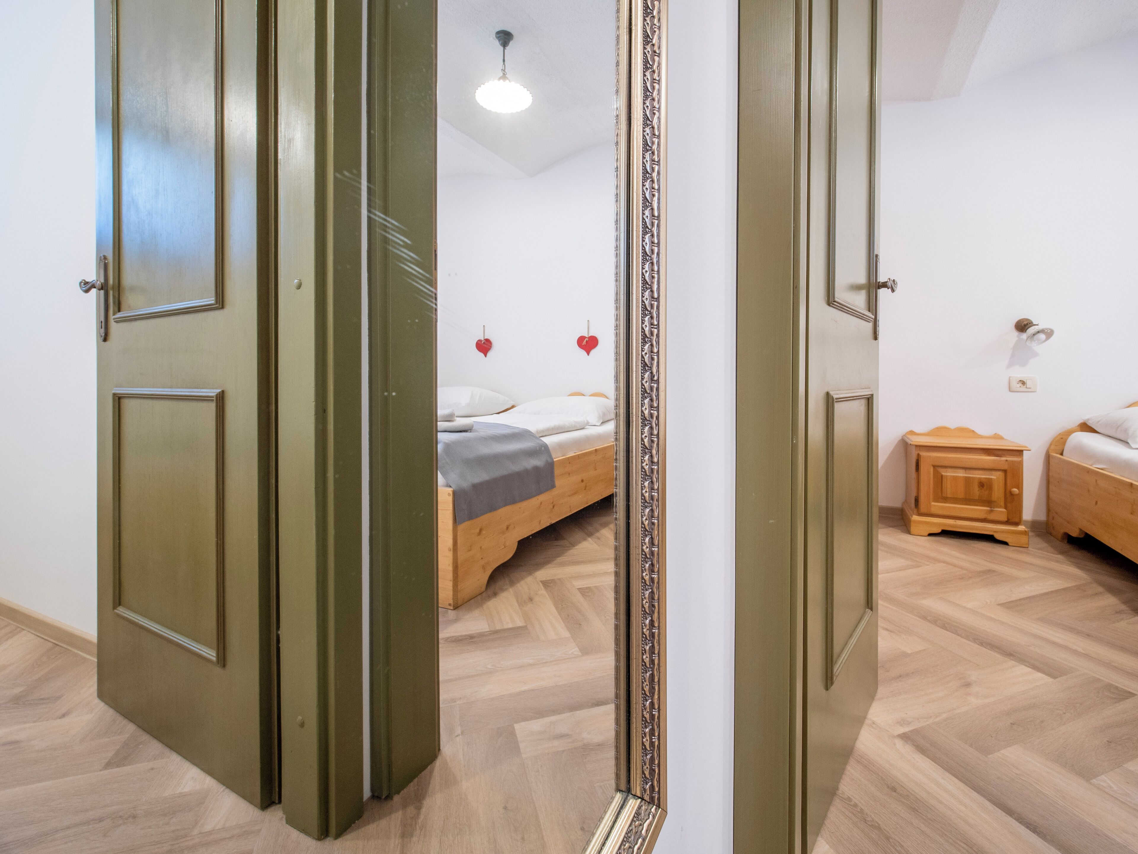 A room with a bed, a wooden nightstand, and a mirror reflecting the room.