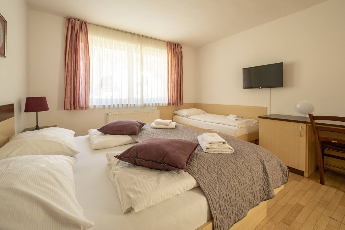 Habitación de hotel con cama, escritorio, televisor y ventana con cortinas.