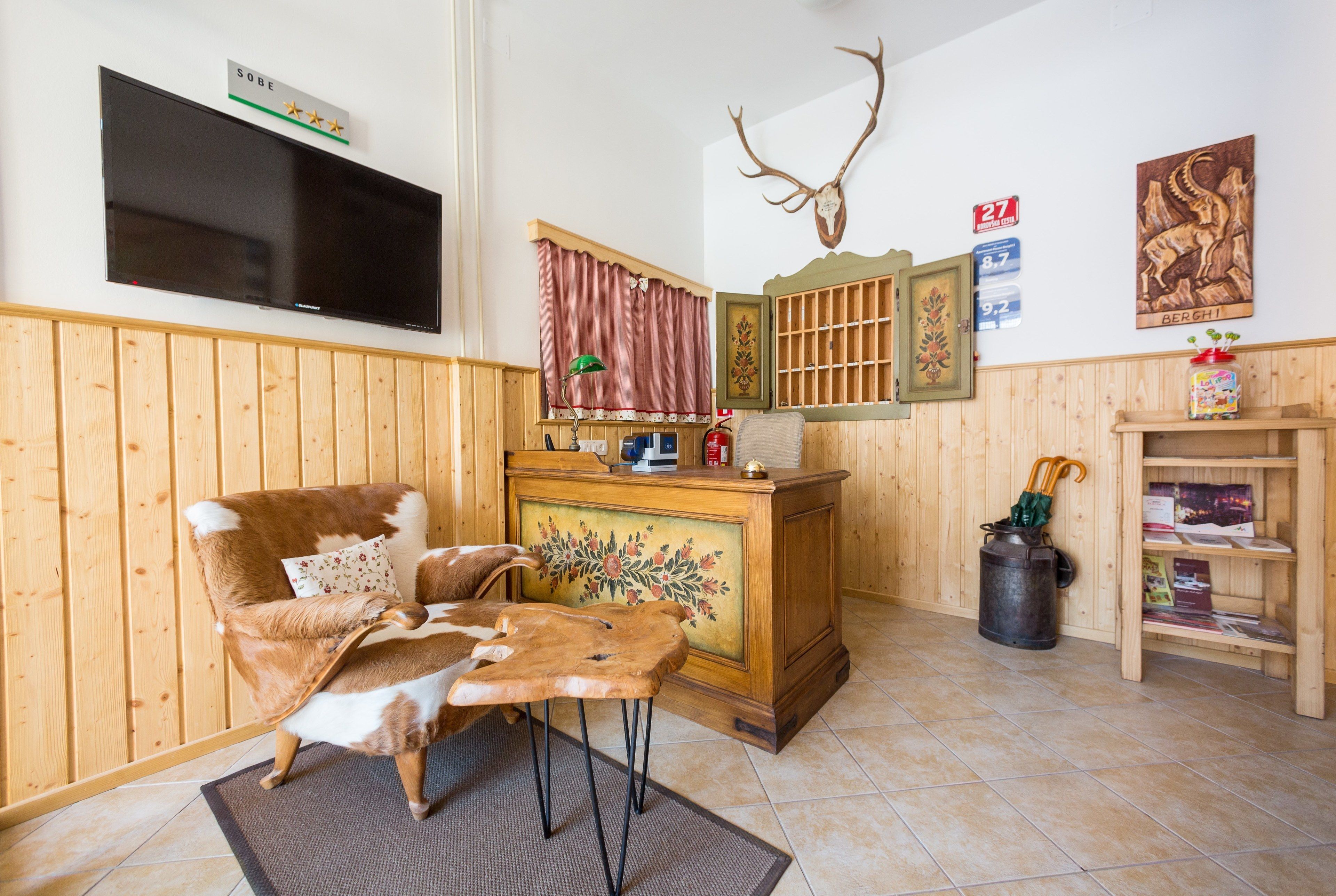 A cozy room with a wooden chair, a flat-screen TV, a deer hide, a fireplace, and a mounted deer head.