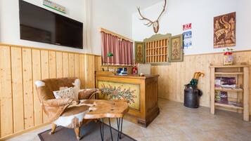 A cozy room with a wooden chair, a flat-screen TV, a deer hide, a fireplace, and a mounted deer head.