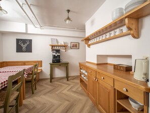 Una cocina acogedora con una mesa y sillas de madera, una cafetera, y estantes con vajilla y una estación de té.