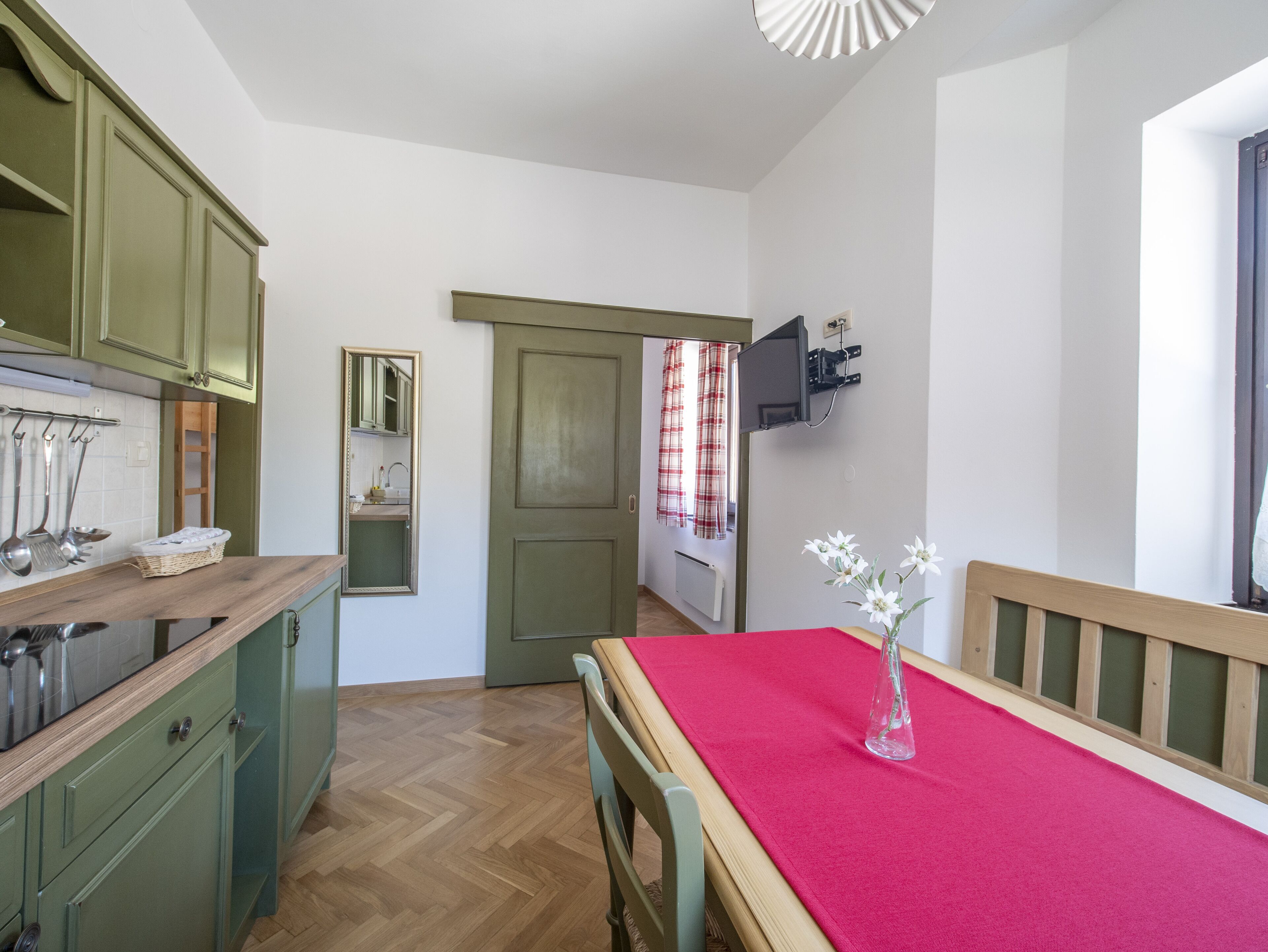 Eine kleine Küche mit grünen Schränken, einer Holz Arbeitsplatte und einer roten Tischdecke.