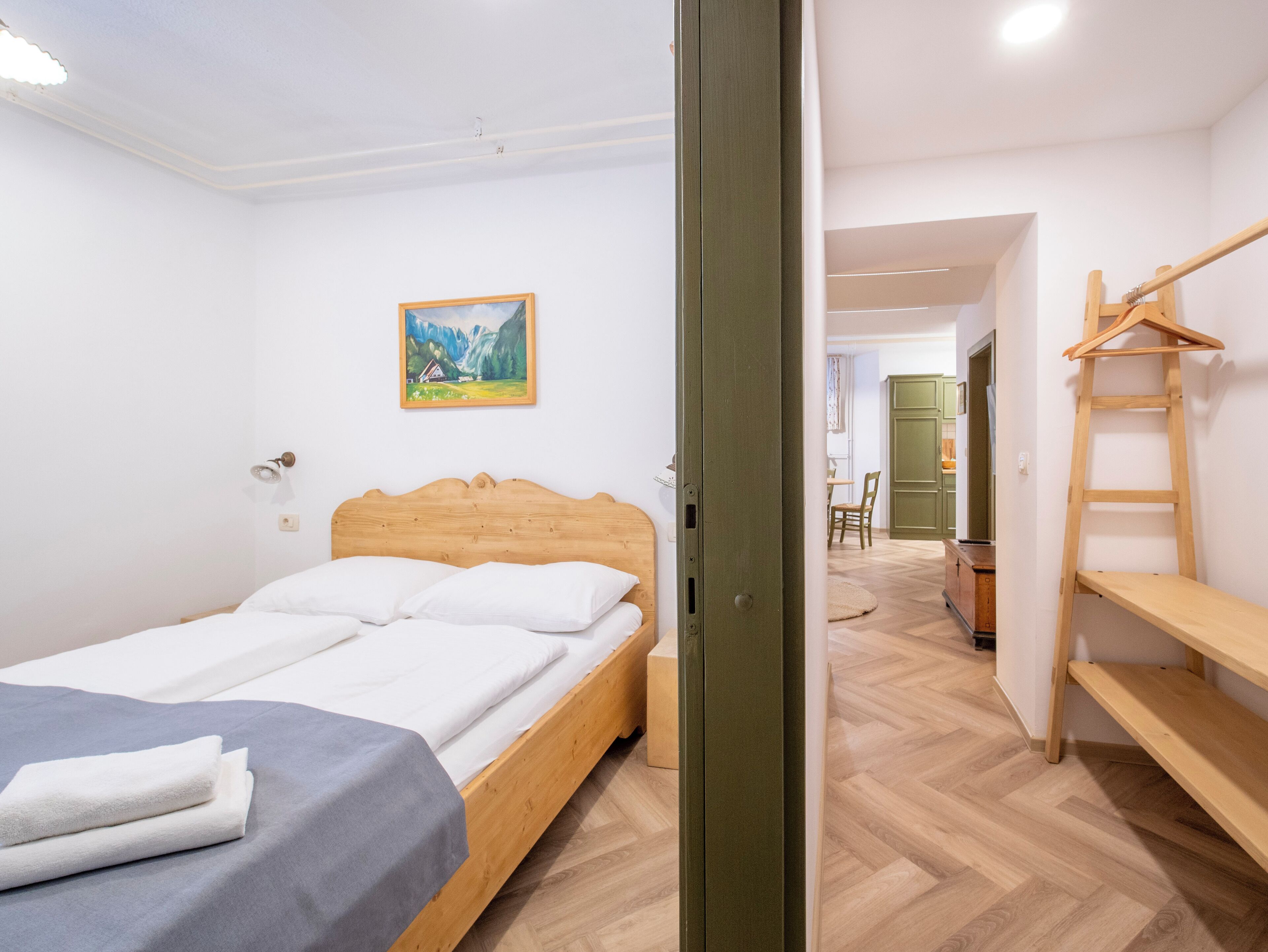 A bedroom with a wooden bed, a painting on the wall, and a wooden shelf.