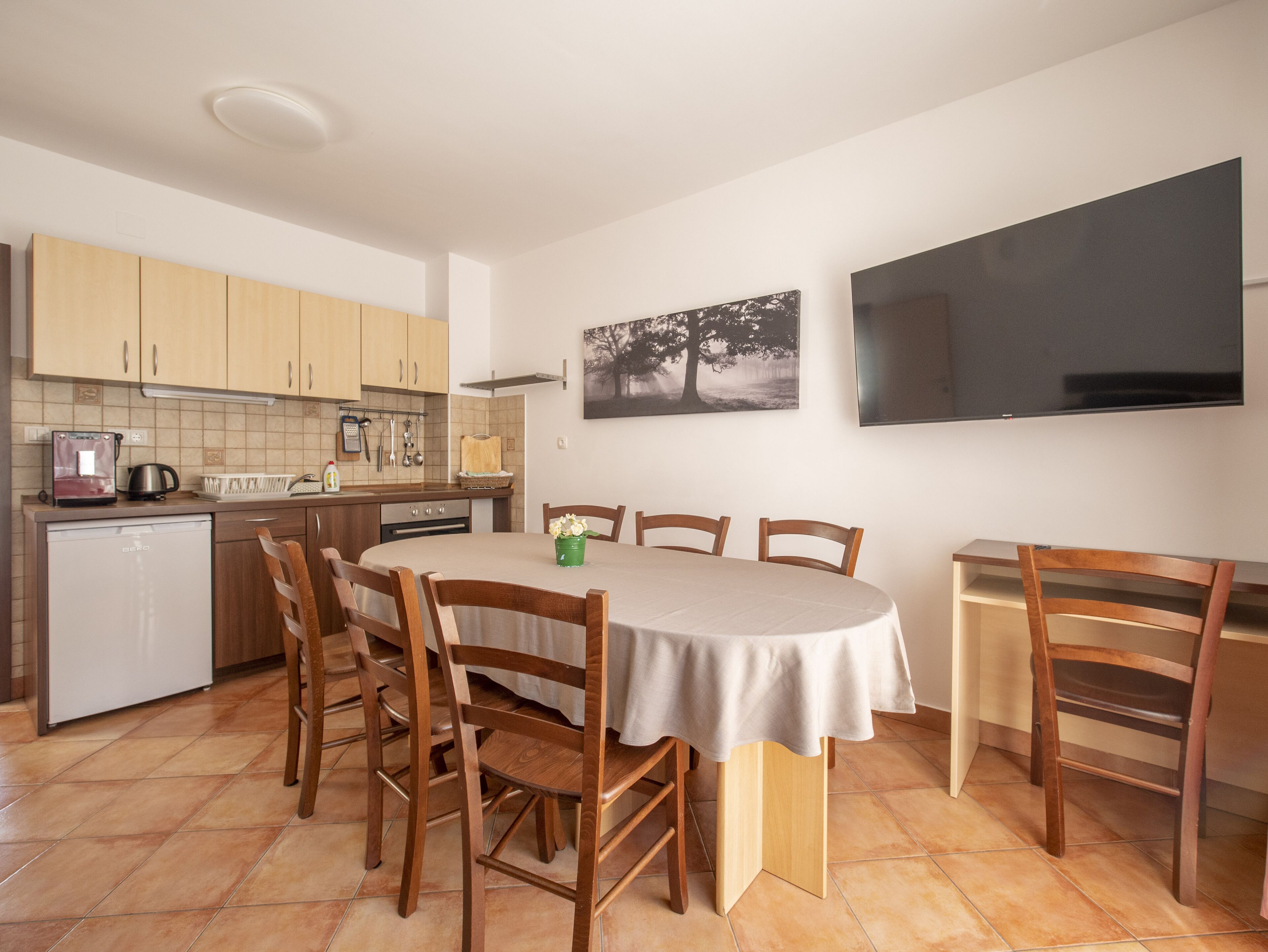 Cocina compacta con armarios de madera, horno empotrado y comedor con mesa y sillas redondas.