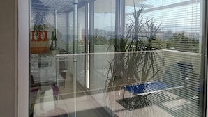 A modern balcony with a glass railing, a potted plant, and a view of the cityscape.