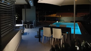 An outdoor pool area with a table and chairs, a large umbrella, and a view of a traditional building in the background.