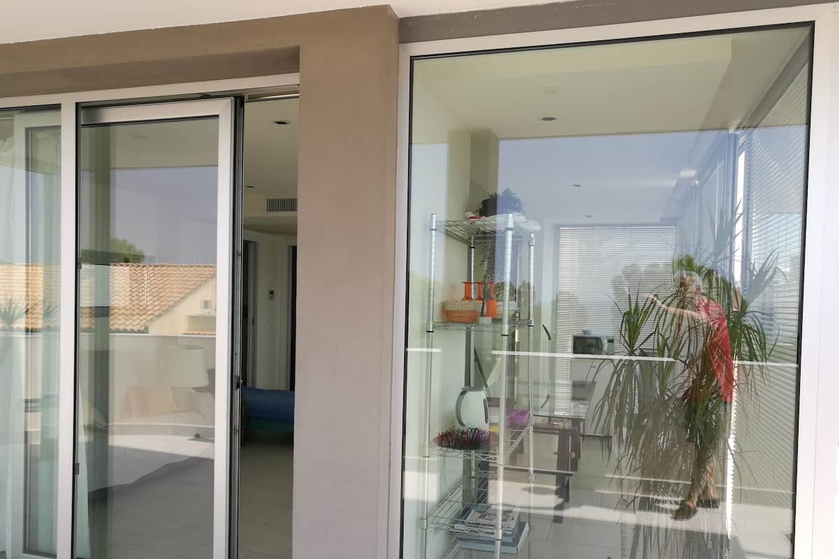 A modern room with a glass door leading to a balcony, a metal shelf with various items, and a potted plant.