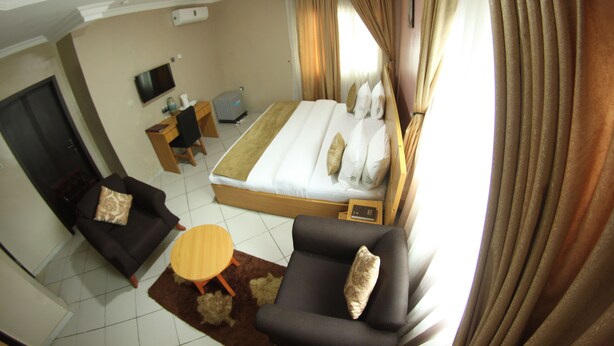 A hotel room with a bed, two sofas, a TV, a desk, and a small table. - Celia's Suites (Abeokuta)