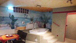 Una habitación con un mural que representa una escena de playa, una mesita con un plato, una silla, una bañera y una puerta.