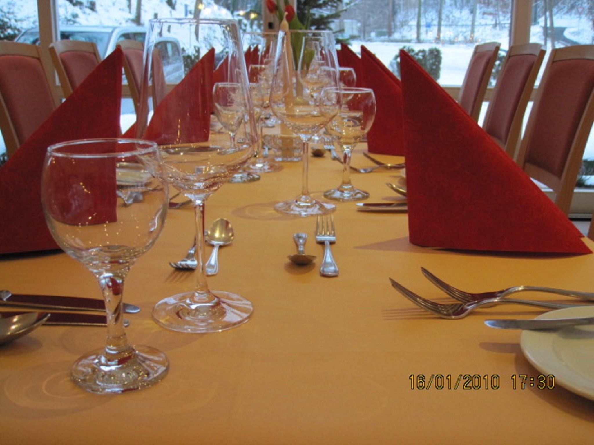 Ein Tisch, festlich gedeckt für ein formelles Dinner, mit mehreren Weingläsern, Besteck und roten Servietten.