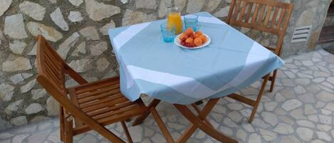 Una mesa con mantel azul, dos sillas de madera, un plato de fruta y un vaso de jugo de naranja.