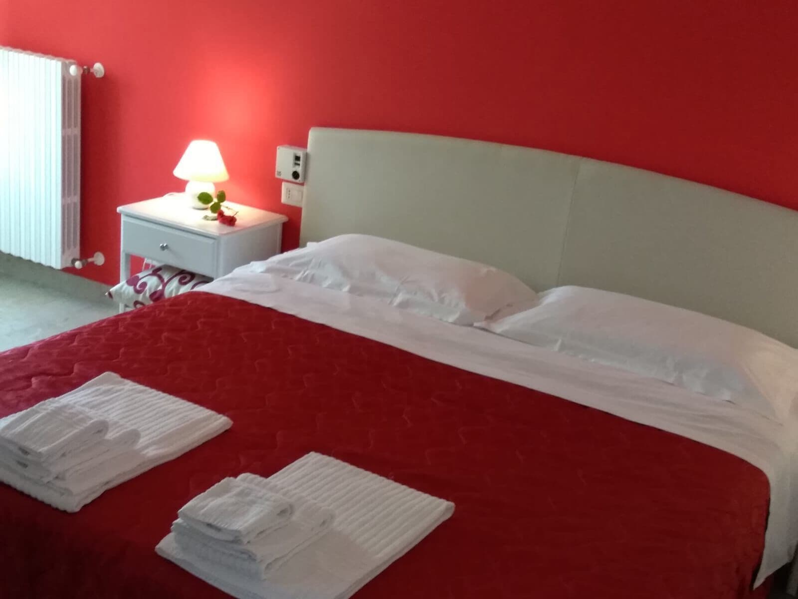 A bed with white linens, a red bedspread, and two folded towels on the bed.