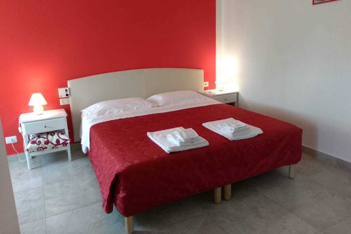 Een net opgemaakt bed met witte lakens en een rode sprei in een kamer met rode wanden en een wit hoofdeinde.
