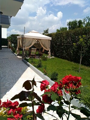 A garden with a tent and outdoor furniture, a stone pathway, and red roses in the foreground.