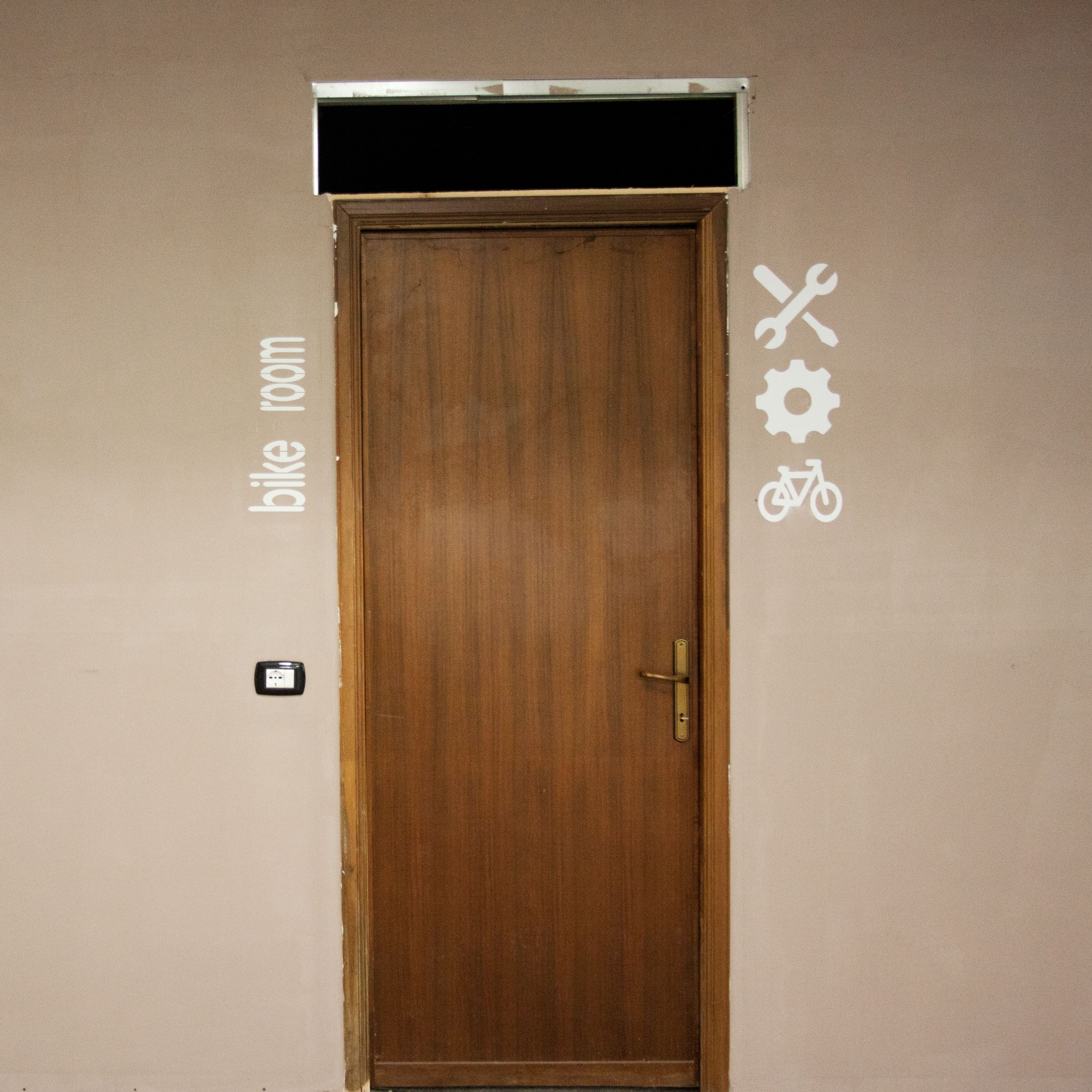A wooden door with a handle and a small electrical outlet on the wall to the left.