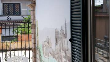 Un balcon orné d’une fresque représentant un bâtiment historique, avec une chaise blanche et une table.