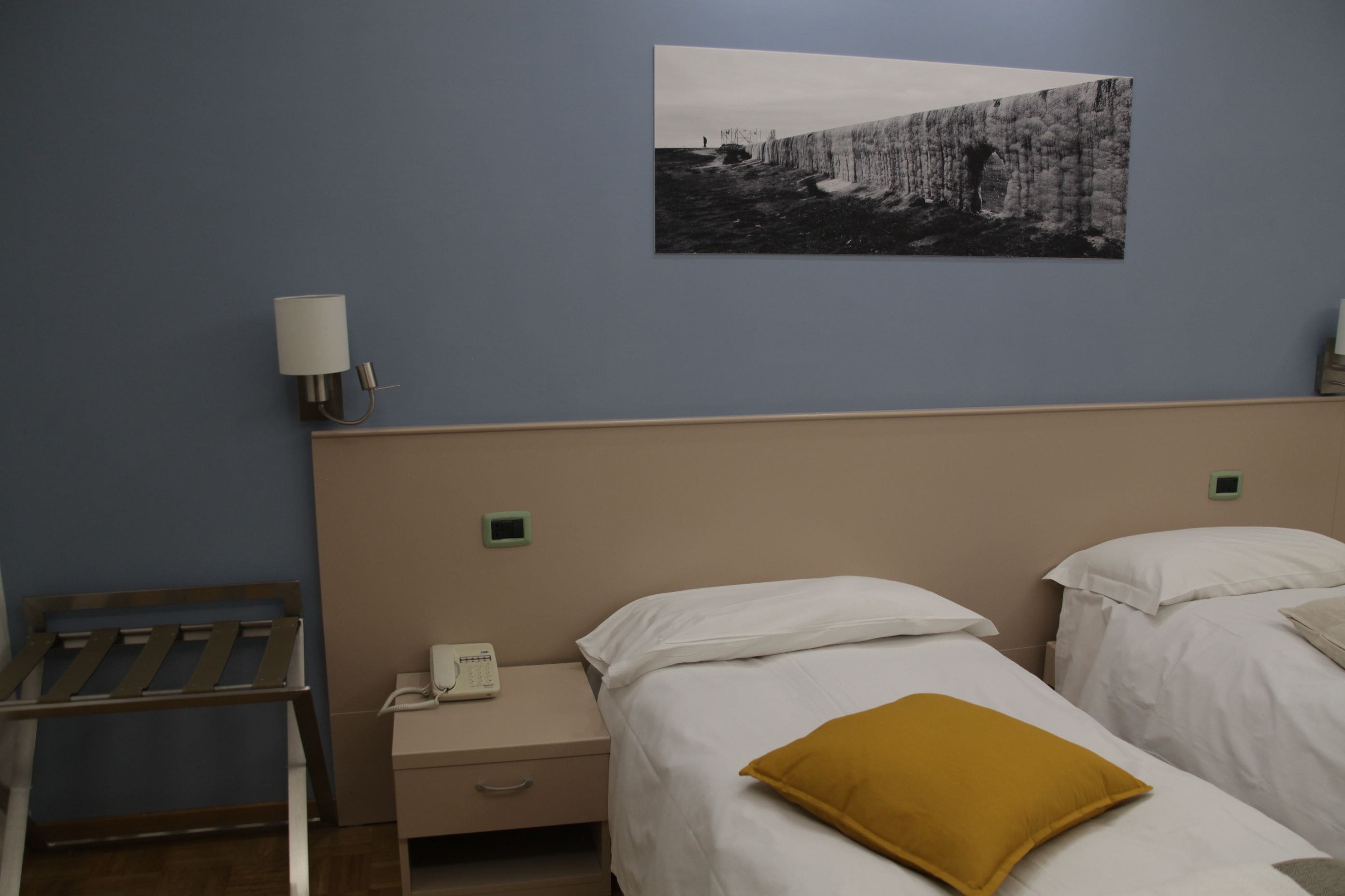 Habitación de hotel con dos camas, una mesita de noche con teléfono, una lámpara de pared y un cuadro en la pared.