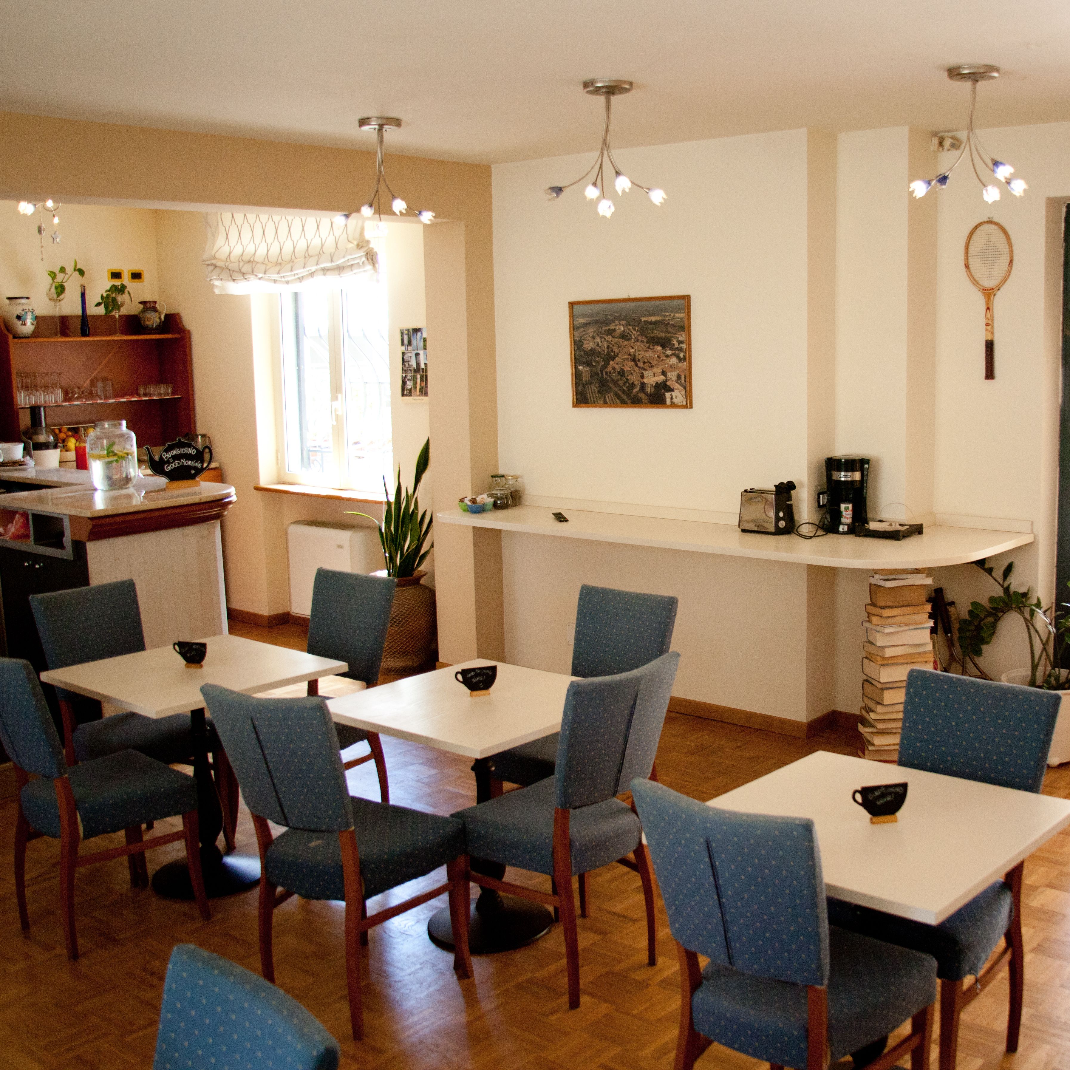 Un comedor con varias mesas y sillas, una zona de cocina con un refrigerador, y una estantería con diversos objetos.