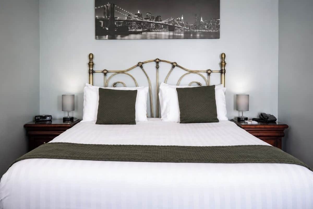 Ein Hotelzimmer mit einem Bett, zwei Nachttischen, Blick auf die Stadt und einem gerahmten Bild an der Wand.