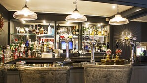 A bar area with a counter, bar stools, and a variety of liquor bottles and glasses. - The Boars Head Hotel (Ashbourne)