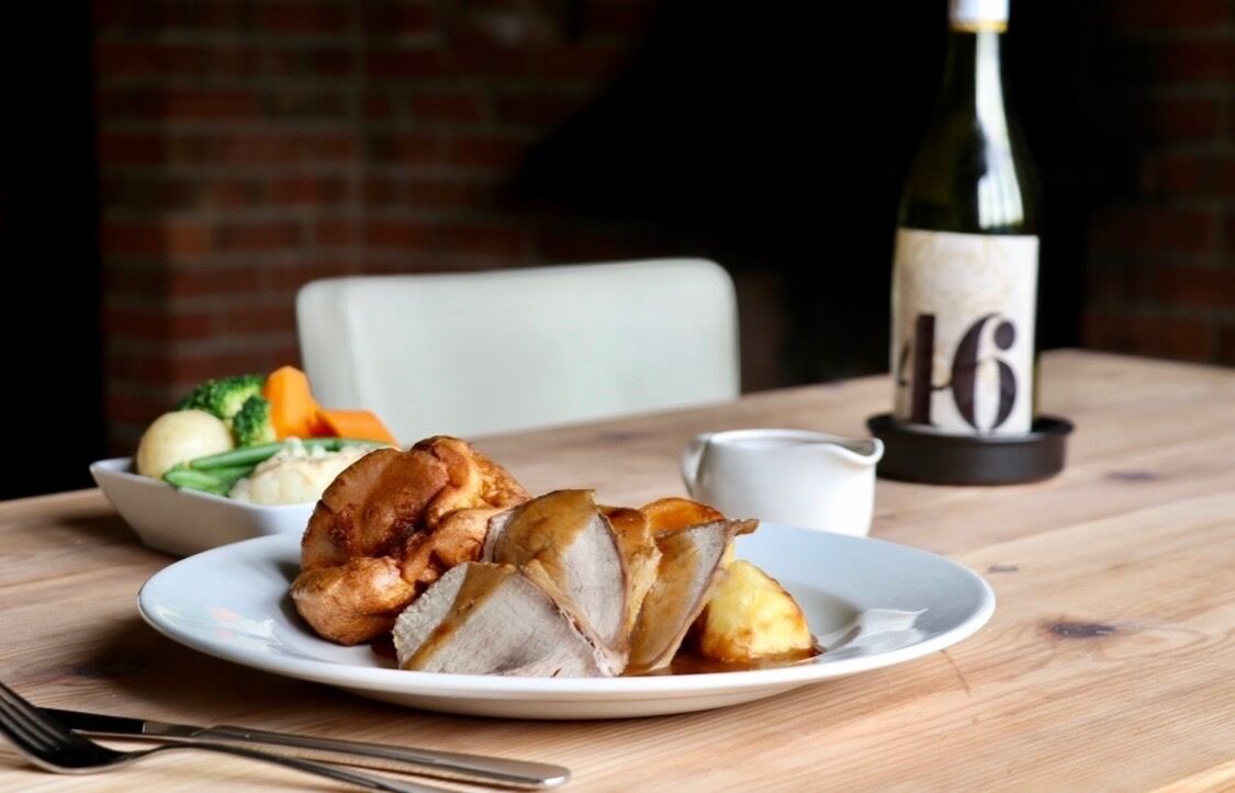 Une assiette de viande rôtie, de légumes et une bouteille de vin, le tout posé sur une table en bois.