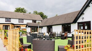 A courtyard with outdoor seating, a table with a bottle, and a wooden fence. - The Boars Head Hotel (Ashbourne)