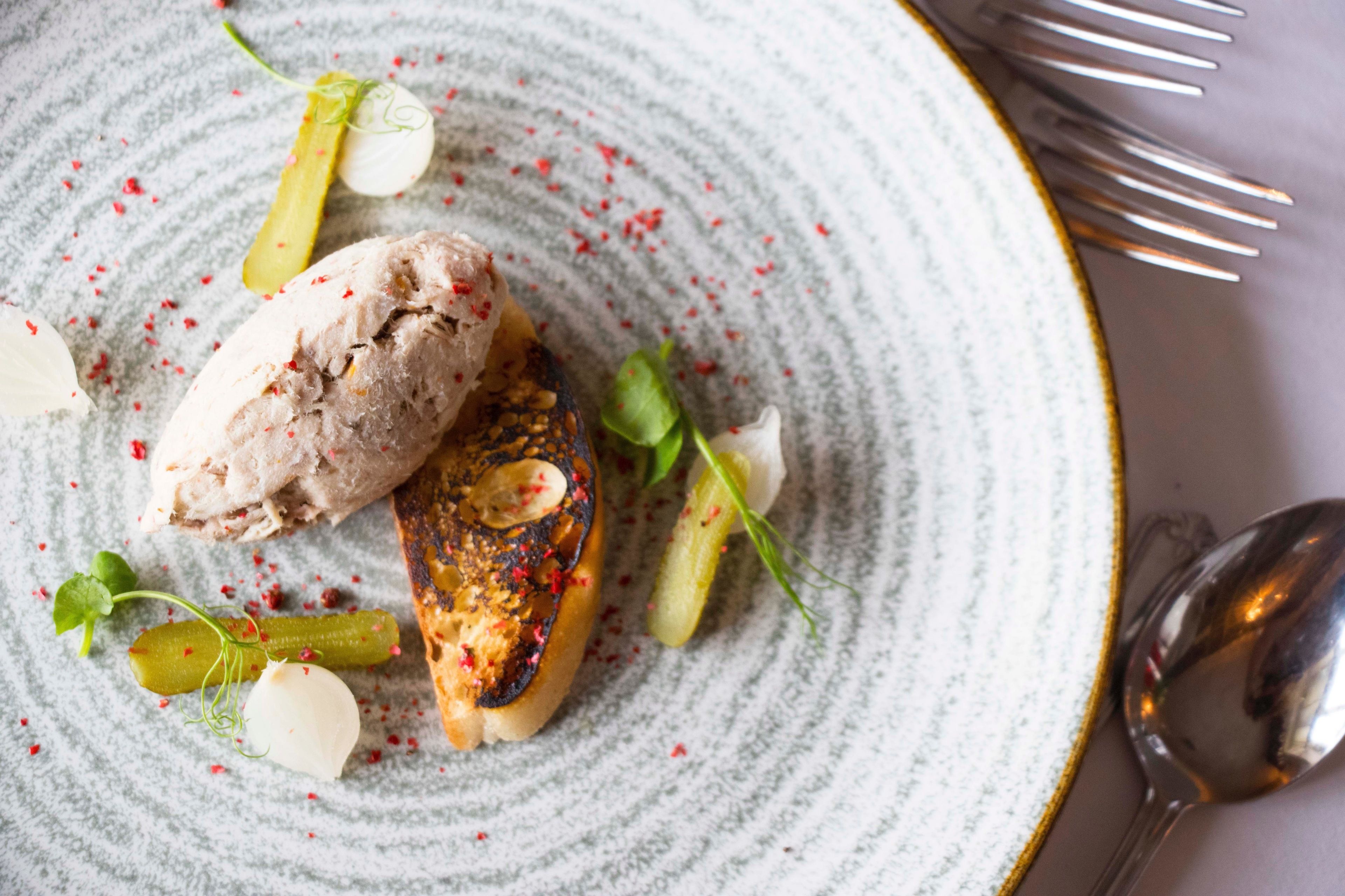 A plate with a grilled item, possibly chicken, garnished with herbs and a slice of pickled cucumber.