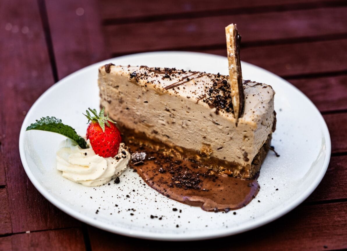 Una fetta di cheesecake con fragola e panna montata su un piatto bianco.
