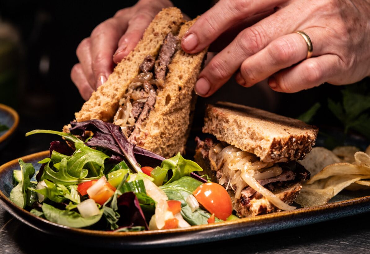 A sandwich with meat and cheese, a side salad, and potato chips on a plate.