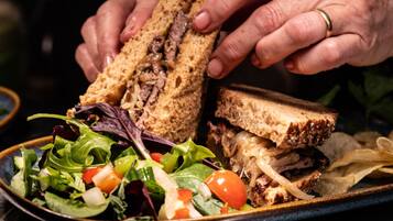 A sandwich with meat and cheese, a side salad, and potato chips on a plate.