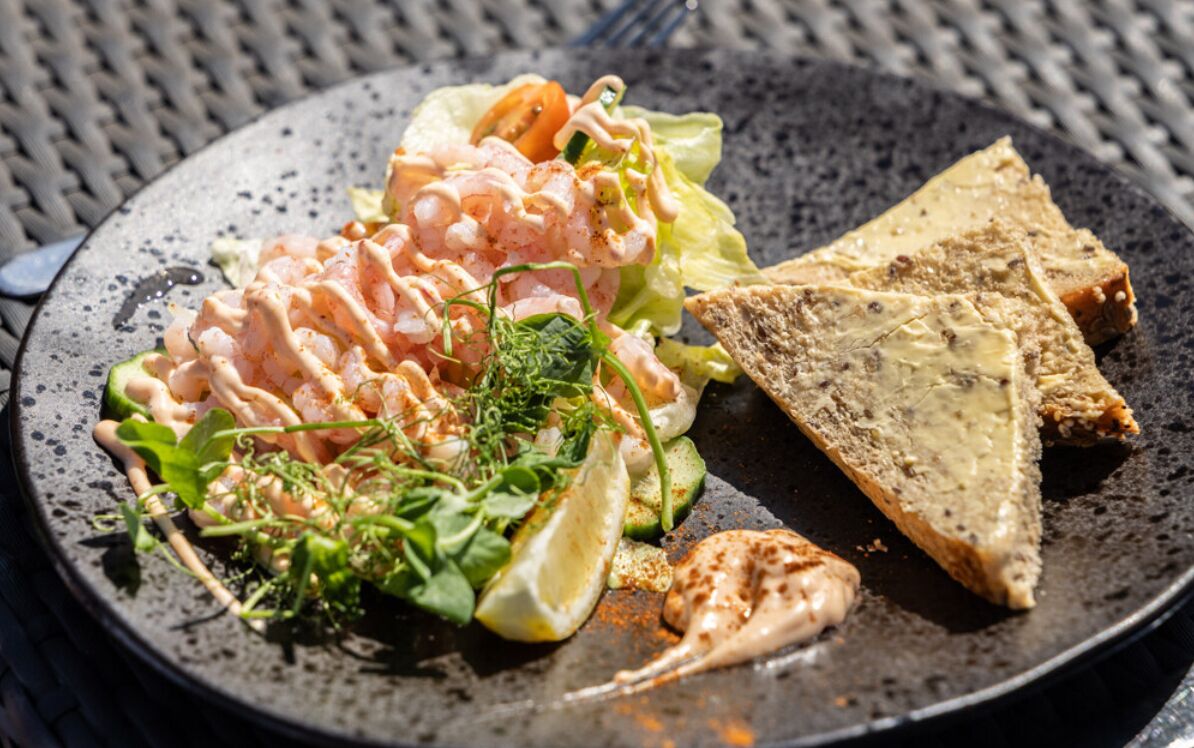 Un plato con ensalada de camarones, lechuga, rodajas de limón y pan tostado.