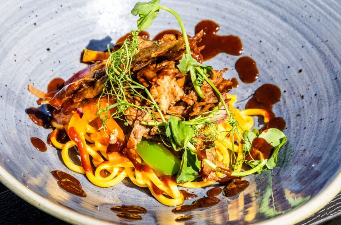 A dish with various vegetables and meat, served on a ceramic plate.