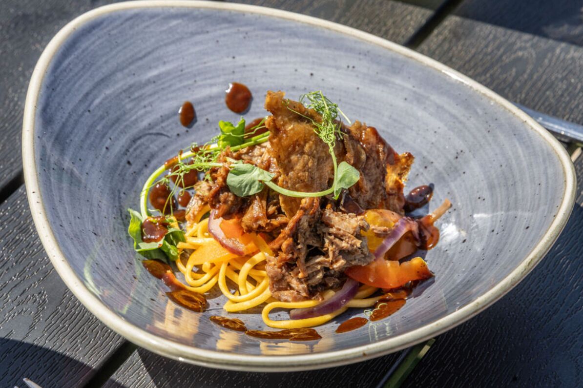Un plato de comida con fideos, carne y verduras sobre un plato de cerámica.