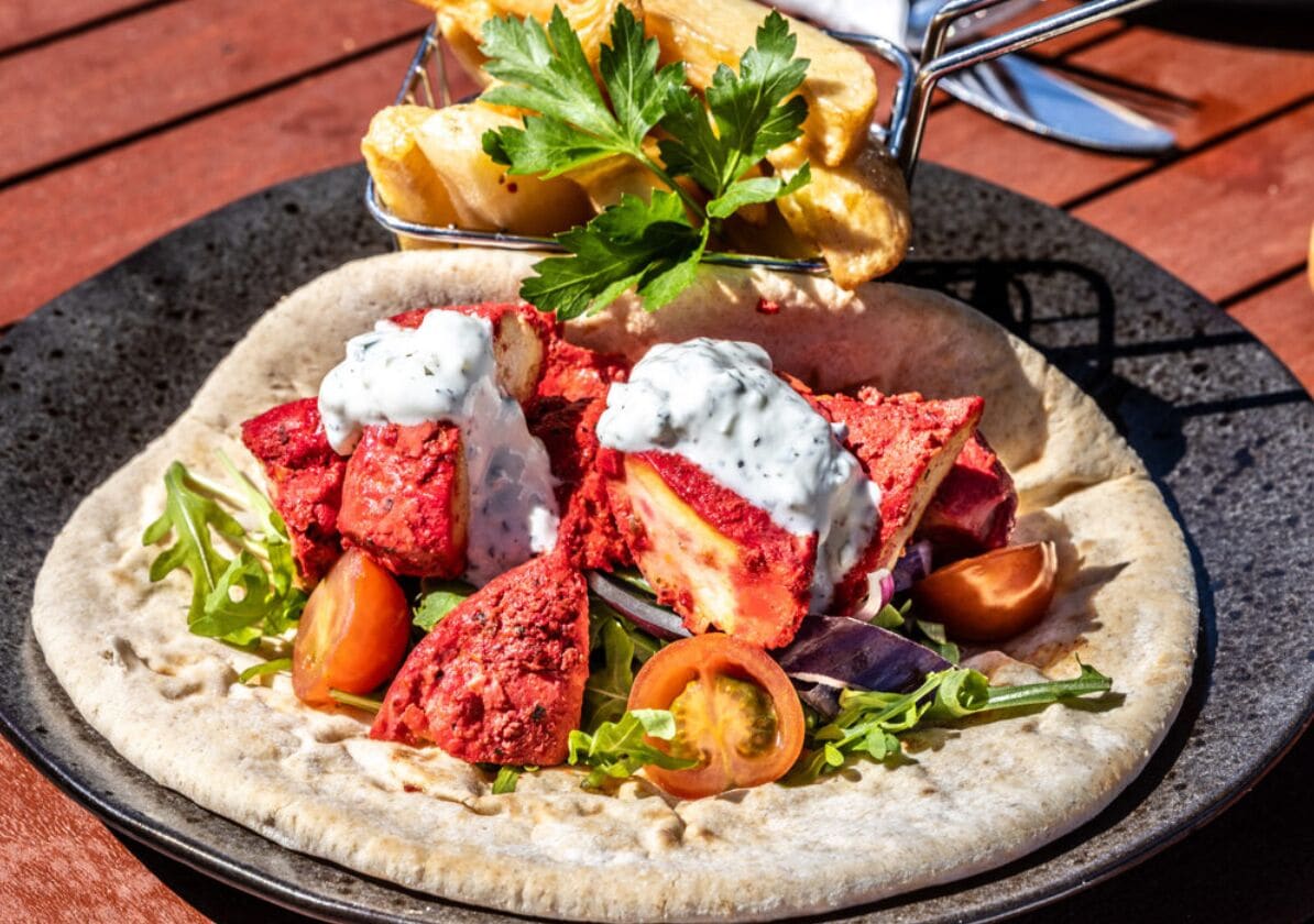 Ein Fladenbrot belegt mit rotem Fleisch, Gemüse und Petersilie.
