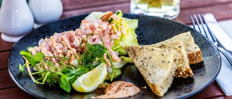 A plate of food with shrimp, greens, and bread on a dark plate.