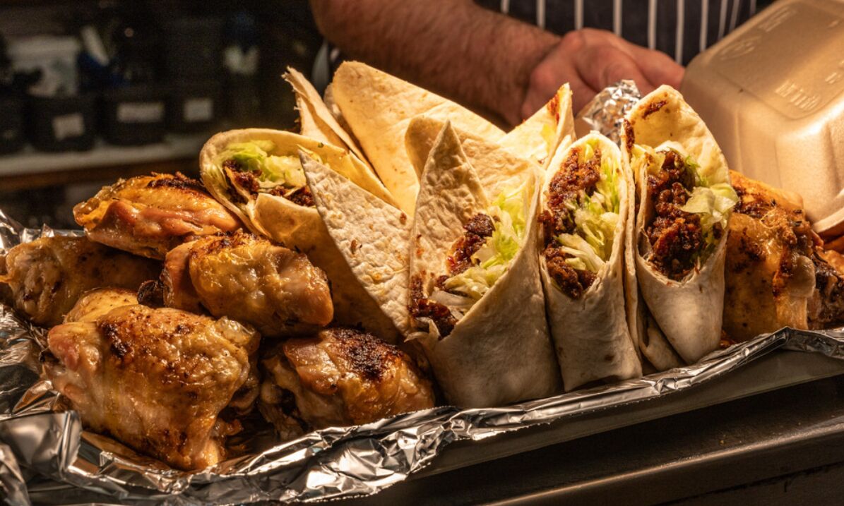 A tray of food including grilled chicken, tortillas, and wraps.